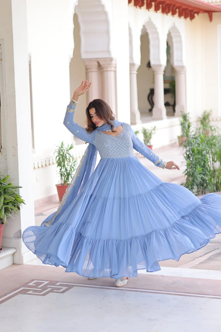 Woman in a blue dress dancing in an outdoor setting with arches and plants.